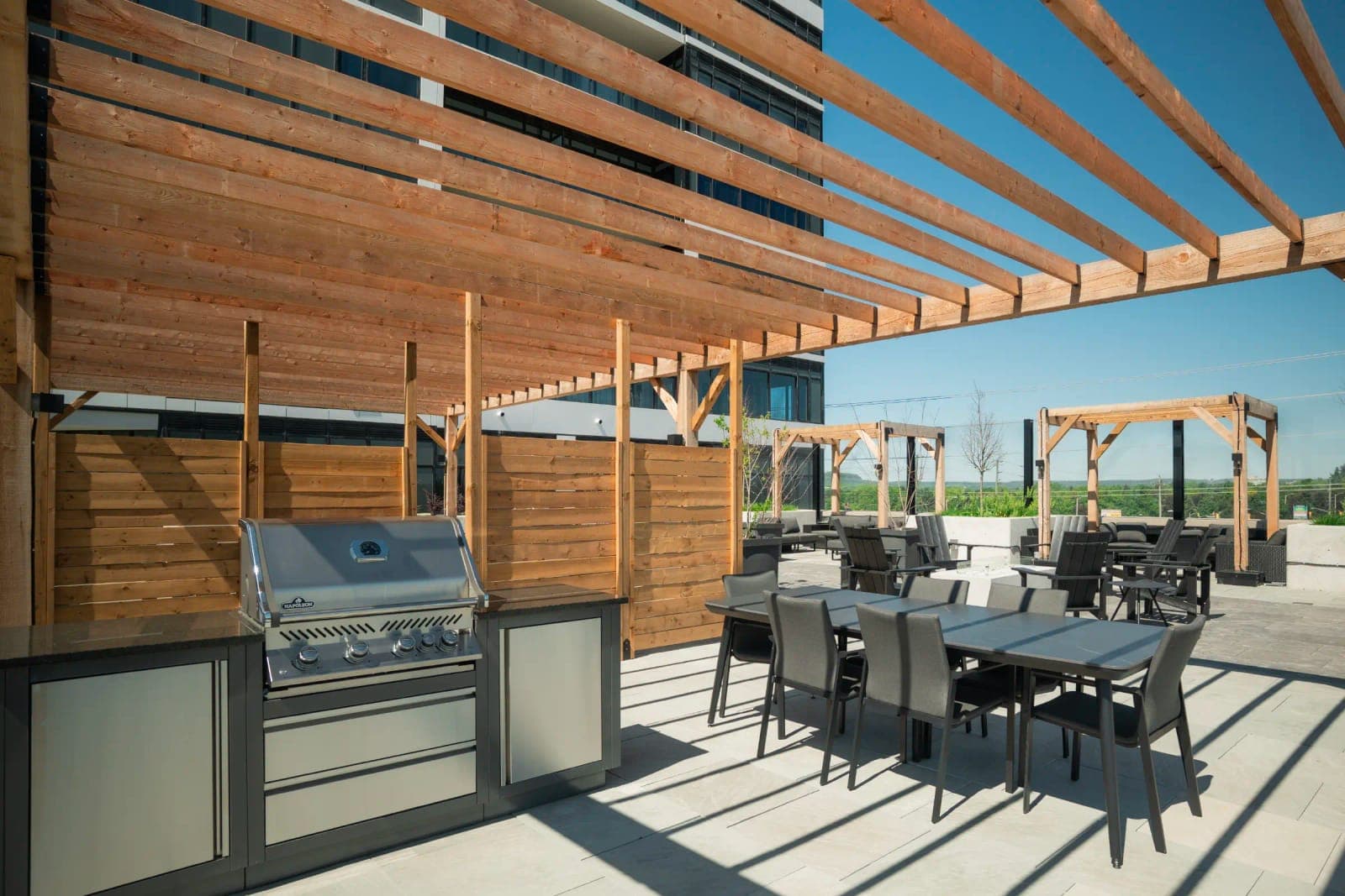 Outdoor kitchen with BBQ and dining tables under pergolas.